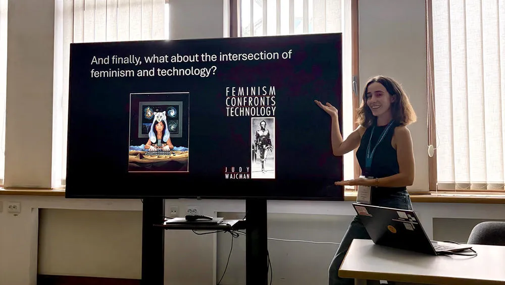 A PhD student is presenting in a room, gesturing towards a screen
