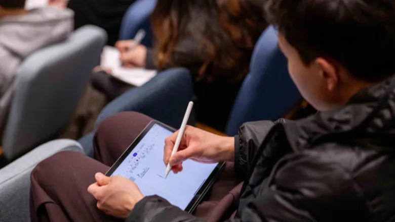 Young man writing on epad in lecture theatre