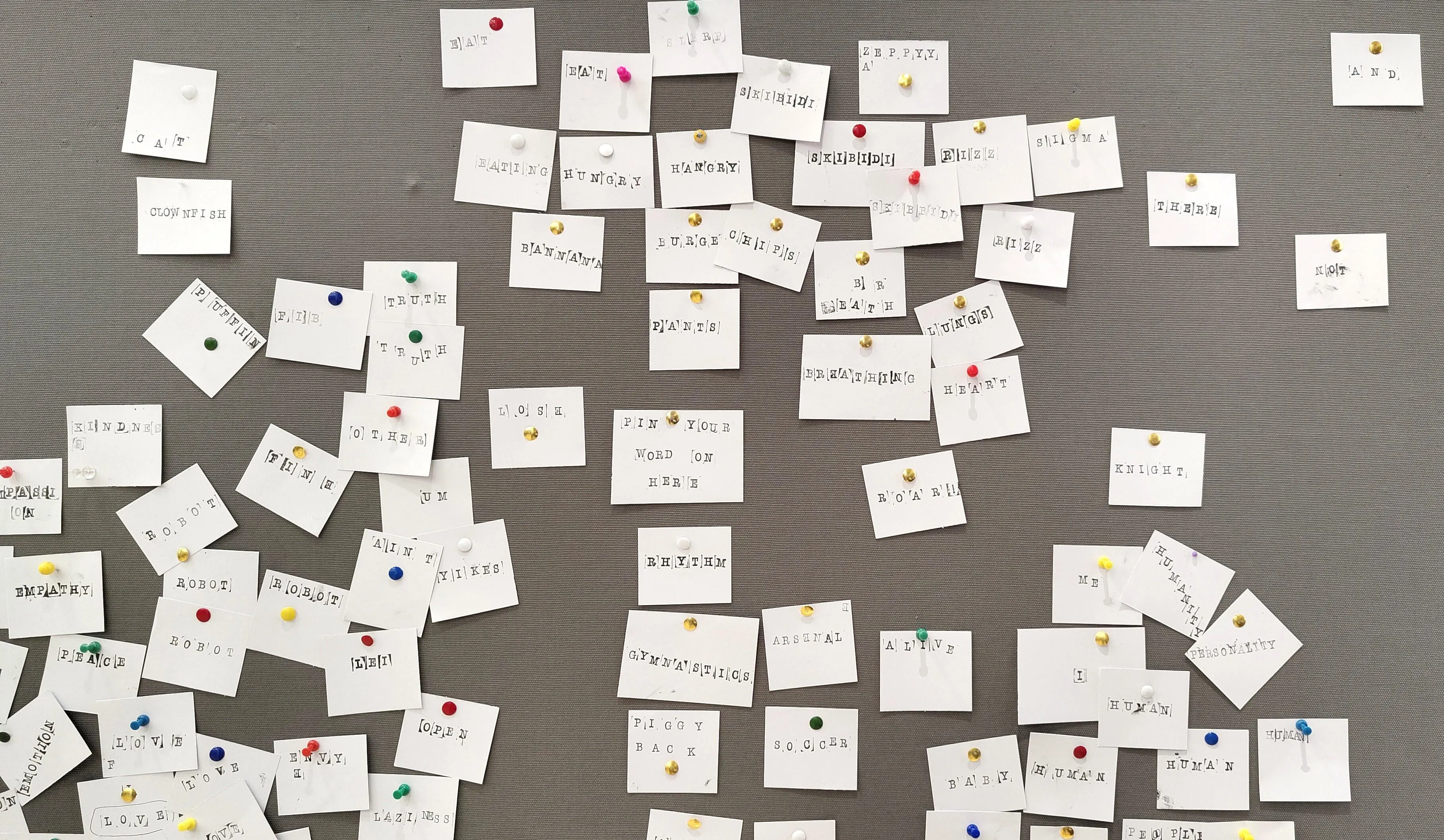 a grey board with white cards pinned on it, with words printed on the cards