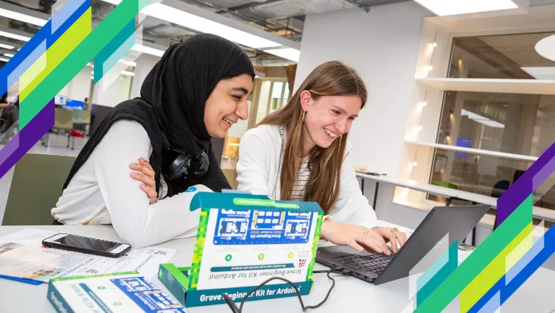 Two students smile as they work together at a laptop computer