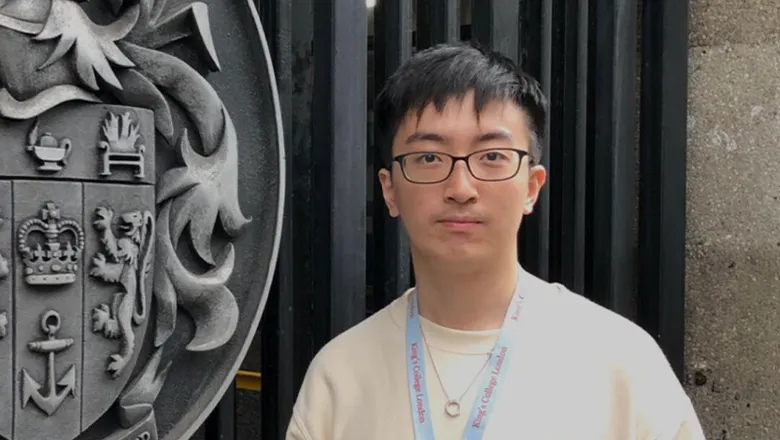 Man standing in front of gate with King's College London coat of arms