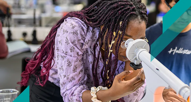 Physics student looking into microscope in a lab