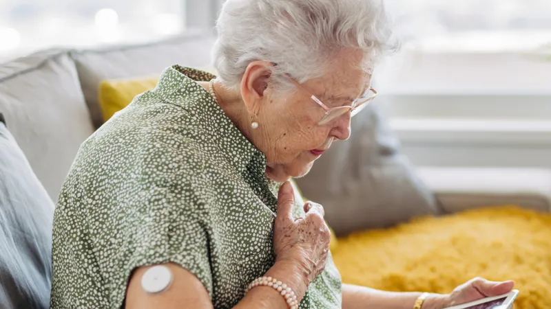An old person with a blood glucose monitor using a tablet computer