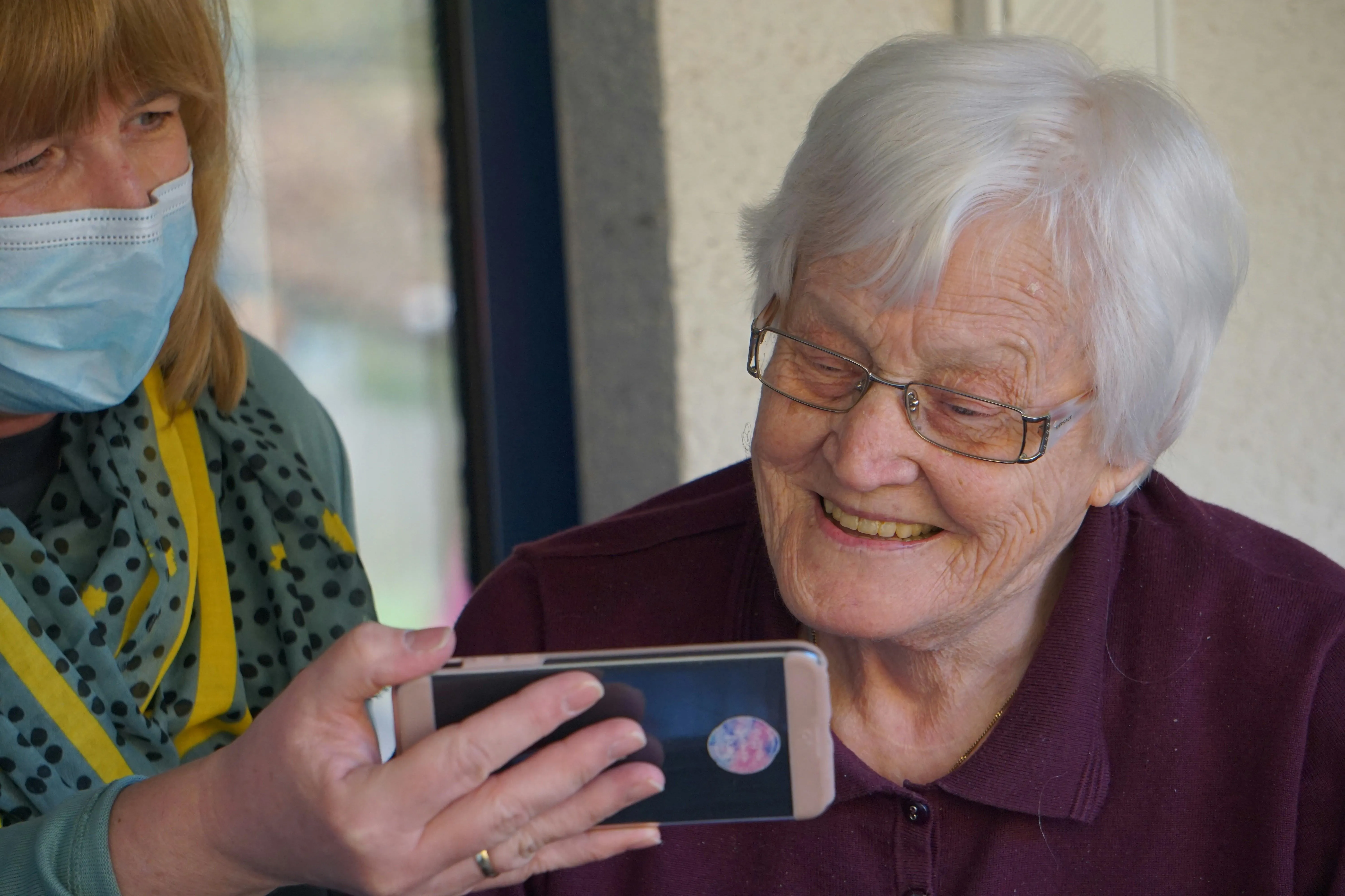 Two women looking at a phone, one is wearing a mask