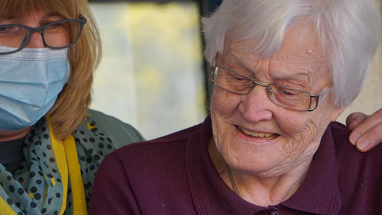 Adult woman wearing a face covering next to an elderly woman. 