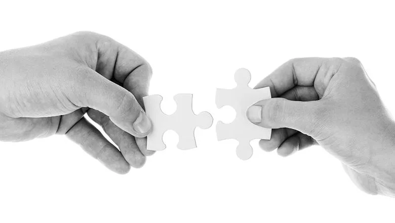 Black and white image of two hands connecting jigsaw pieces