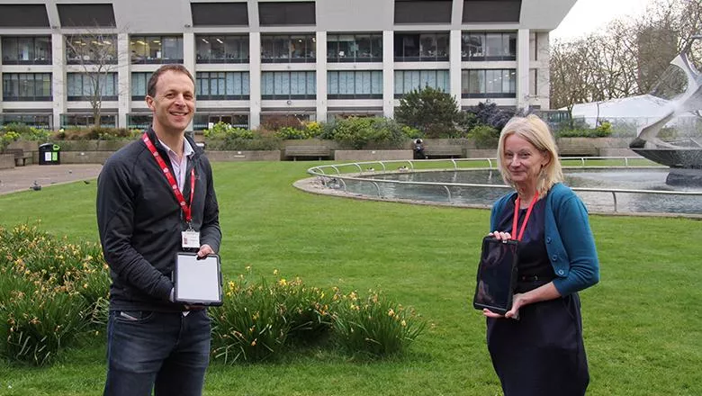 Joel Meyer and Louise Rose holding tablet devices outside St Thomas' Hospital in London.
