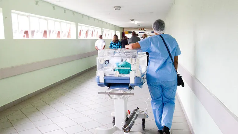 Baby in incubator pushed down corridor by health professional