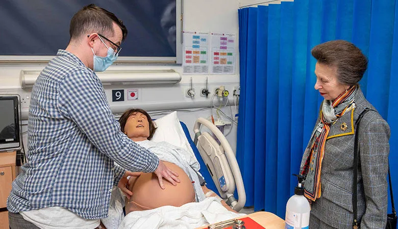 Princess Anne and a technician standing next to a clinical simulation mannikin lying on a bed