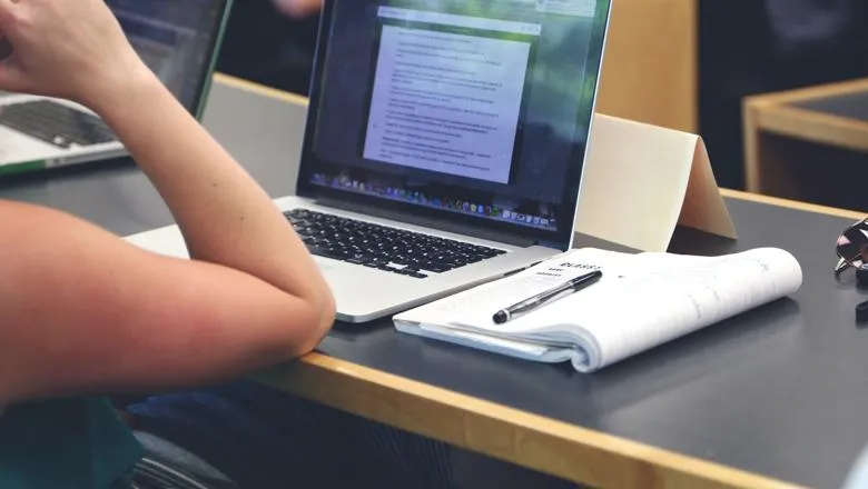 Student in lecture with laptop and notepad