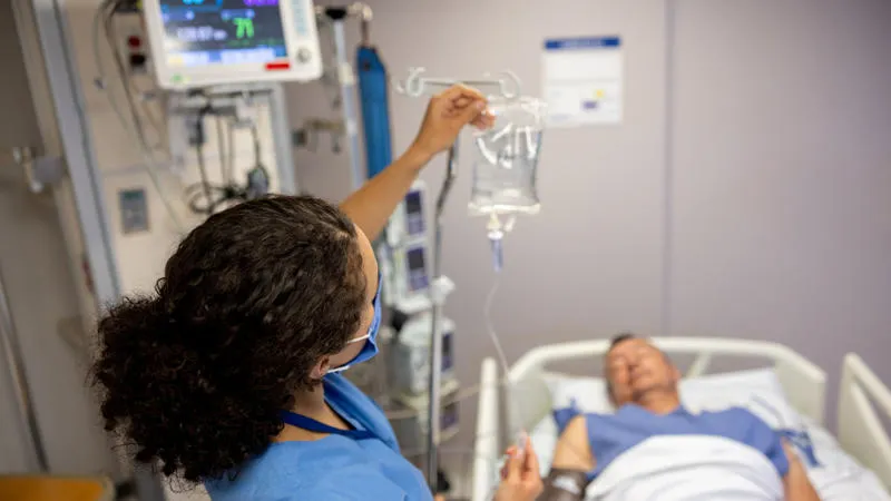 Person lying in hospital bed being treated by a nurse with an IV drip.