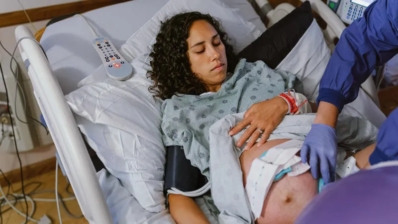 Pregnant person lying in a hospital bed with a nurse taking an ultrasound of the lower stomach