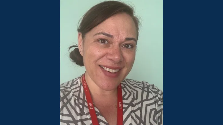 A woman with a side bun smiles taking a selfie, wearing a patterned white and brown shirt.
