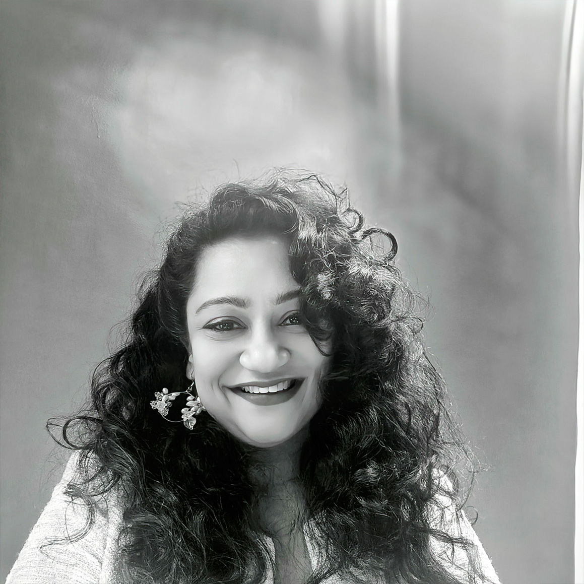 A black and white photo of Payal Saxena with long dark curly hair, dressed in a light coloured shirt.