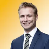 A picture of King's College London graduate Luca Brockmann. He is wearing a navy suit and a grey and black striped tie.