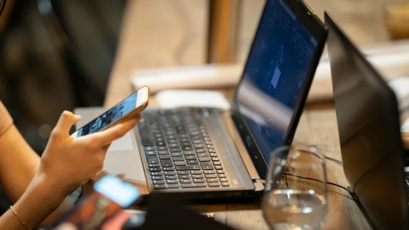 Someone working on a laptop, scrolling on their phone