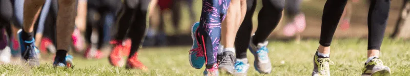 Several people in colourful sports shoes running through a sunny field.
