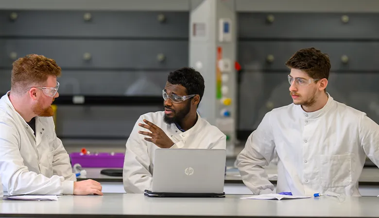Three students in lab gear, in conversation