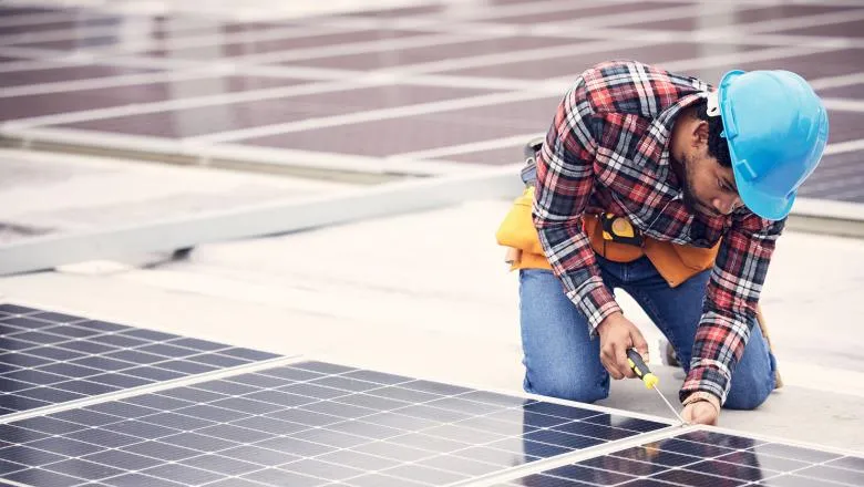 Black man installing solar panels on a roof