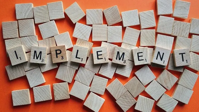 Scrabble titles spelling out "implement" on top of blank tiles and an orange background