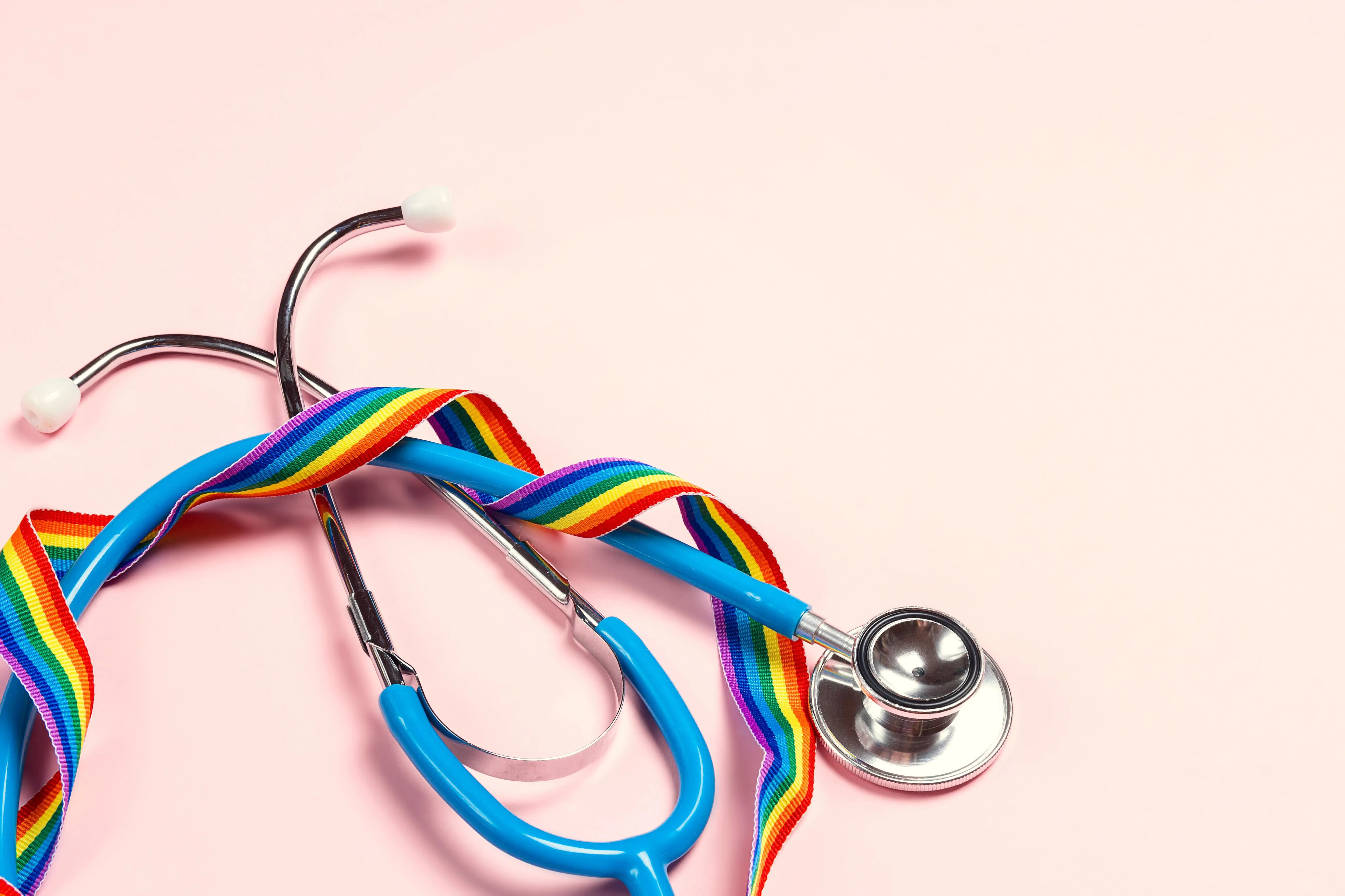 A stethoscope with a rainbow ribbon on pink background.