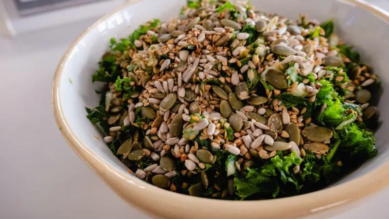 A white bowl of rubbed kale, fennel and mix seed salad