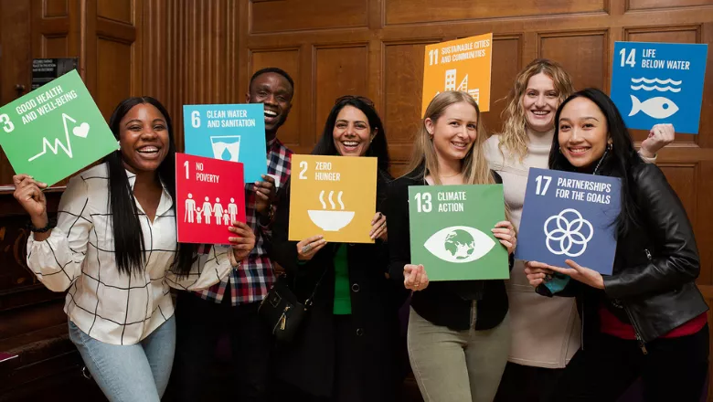 students smiling and holding up brightly coloured boards featuring different UN Sustainable Development Goals