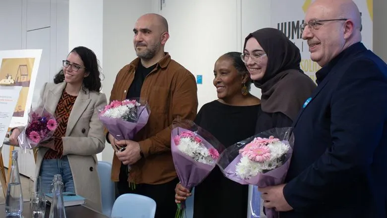 Experts smile after a panel discussion and hold bouquets of pink and white flowers. 