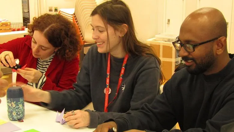 Three people make origami birds at a workshop