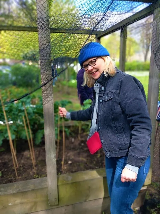 Stephanie wearing a blue hat standing in front of a raised garden bed at Coin Street Neighborhood's Community Garden. 