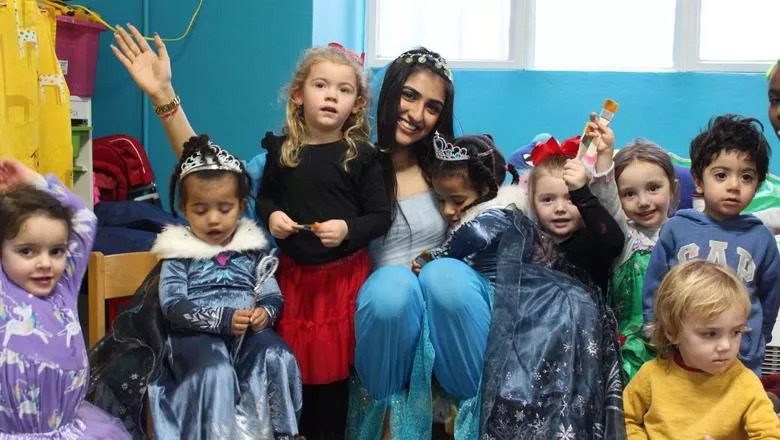 A volunteer dressed as a princess sits with 7 young children - some are also dressed as disney princesses