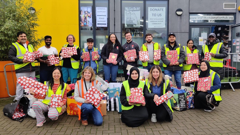 Group of individuals standing infront of a donation centre holding Christmas Gifts.