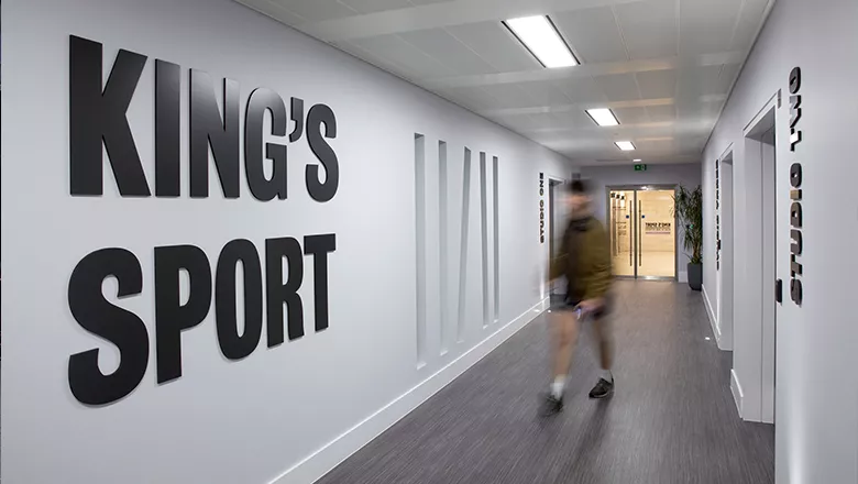 Member walking out of gym studio pass 'King's Sport' Signage. 