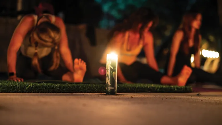 A candle ininfront of a group of individual taking part in yoga in a dark room. 