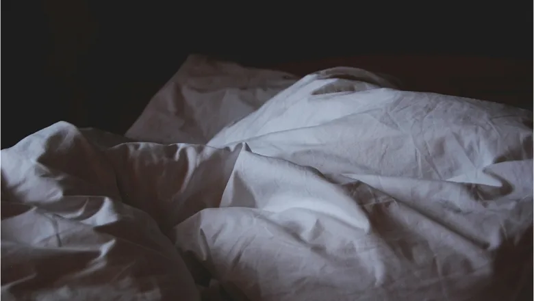 A bed with messy bed linen in a dimly lit room 
