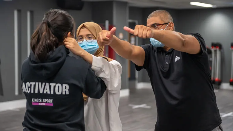 Two students learning self-defence techniques from teacher.