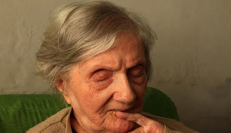 An elderly woman with eyes closed, sitting in a chair