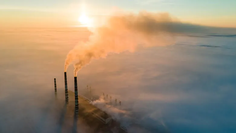 A cloud of emissions floats from a factory or power station's tall chimney stacks