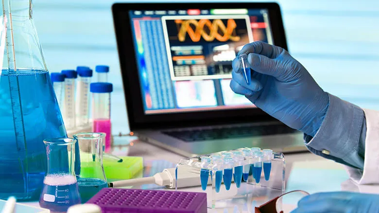 Scientist holding test tube and working with laptop in genetics lab