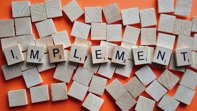 The letters 'implement' spelled out in wooden tiles