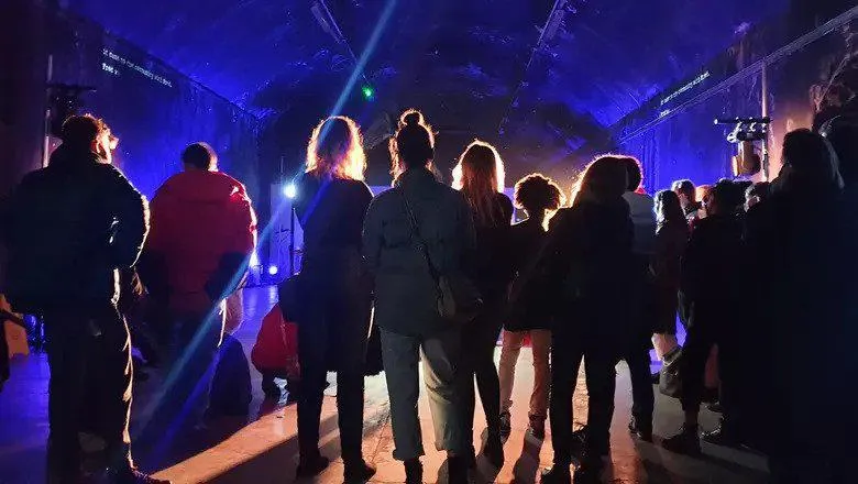 Group of people, backs towards us, standing looking towards light