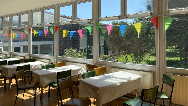 Tables with tablecloths and chairs and bunting hanging in the window on a sunny day