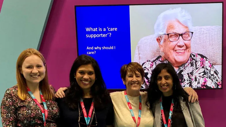 Four people standing in front of a screen showing someone smiling