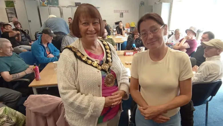 Two people, one with a mayoral chain, in a room with other people sat at tables