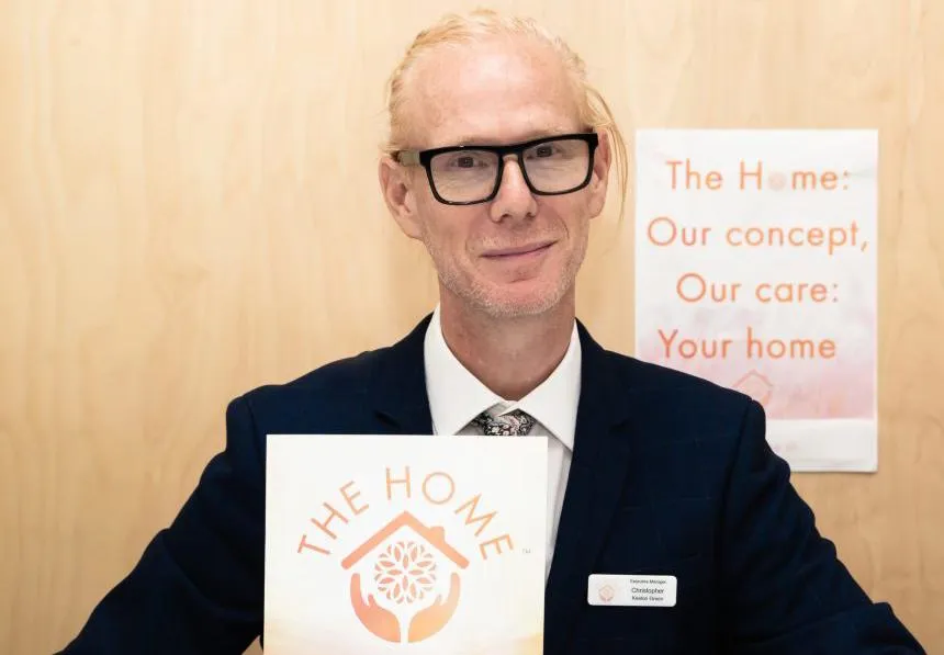 Photo of Christopher Green holding a document with 'The Home' printed on it