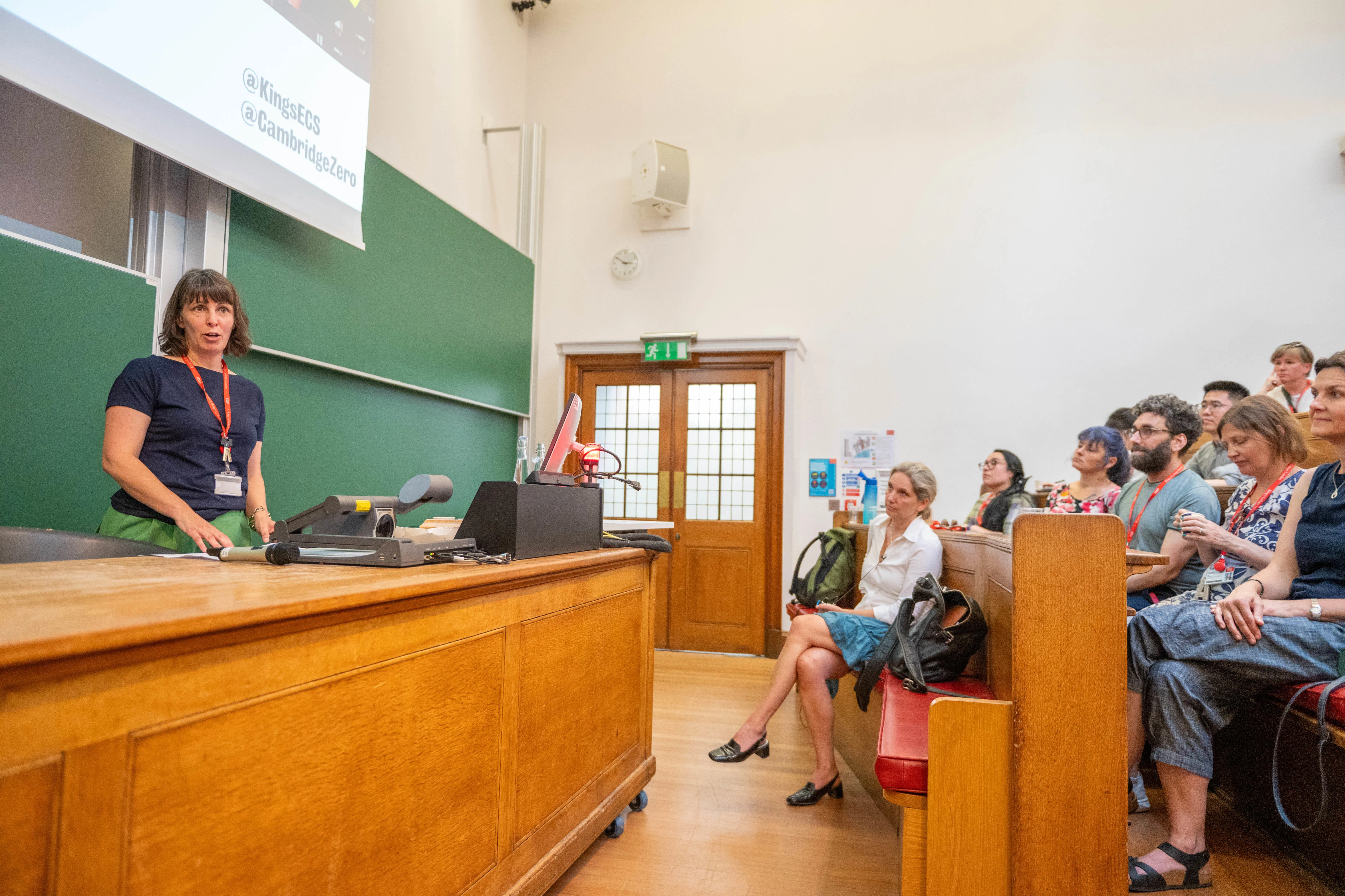 a white woman white short black hair and a fringe talks to a room of engaged academics