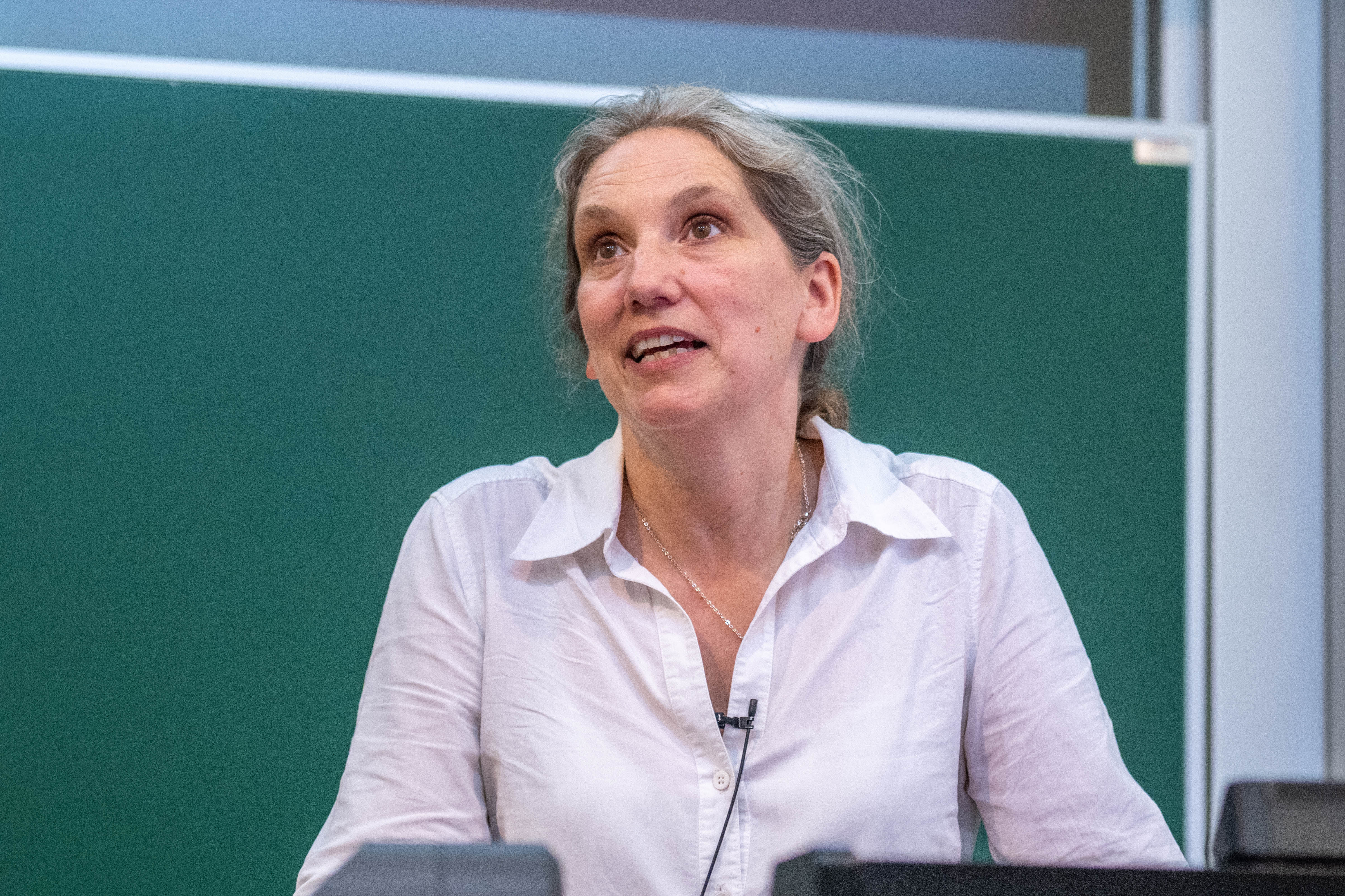 a white woman with blonde grey hair wearing a white shirt delivering a speech