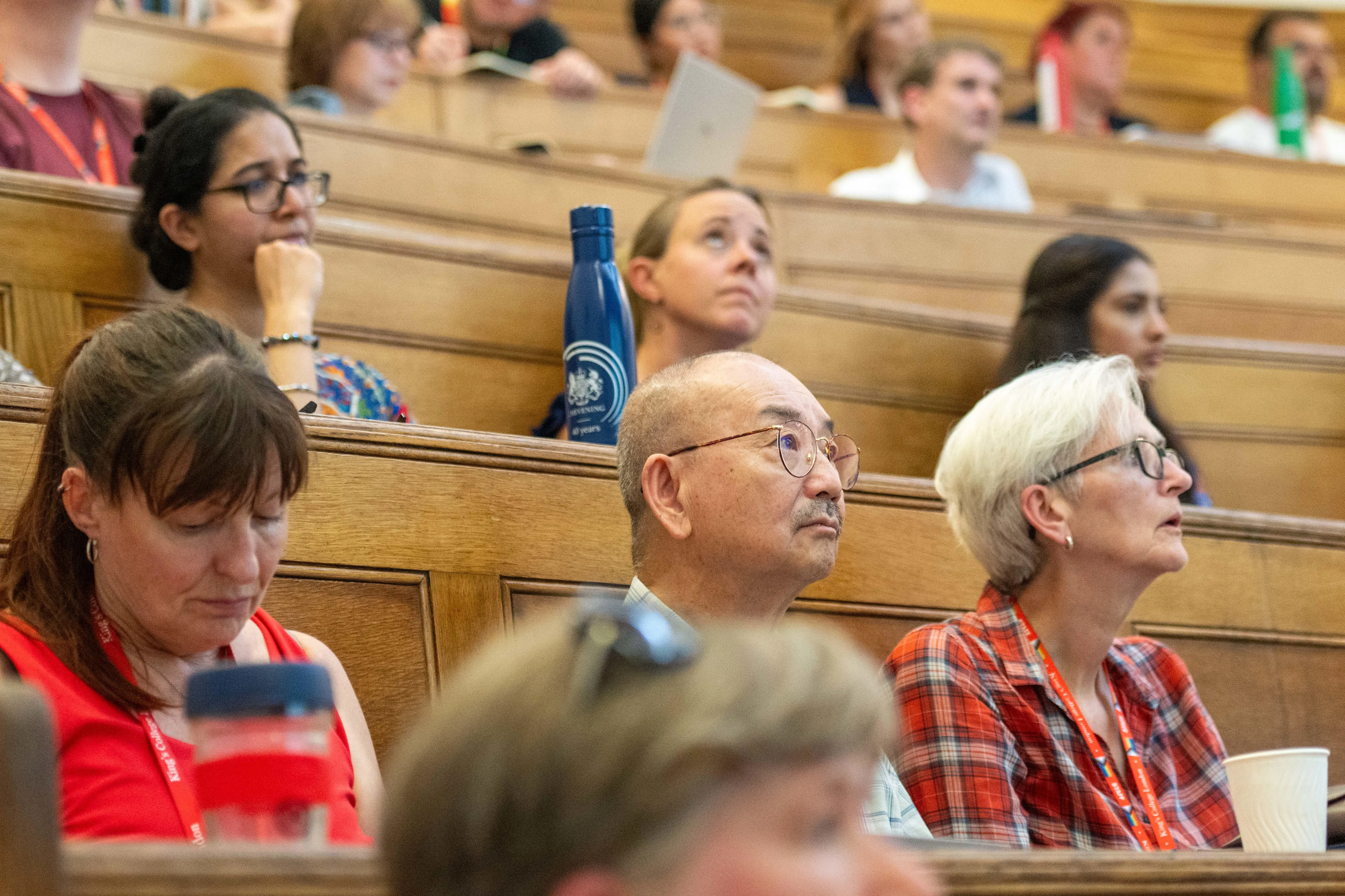 audience at a lecture including white woman with glasses and short blonde hair, asian man with glasses