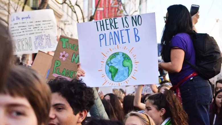 People in an environmental activism demonstration, raising a sign written 'there is no planet b'.