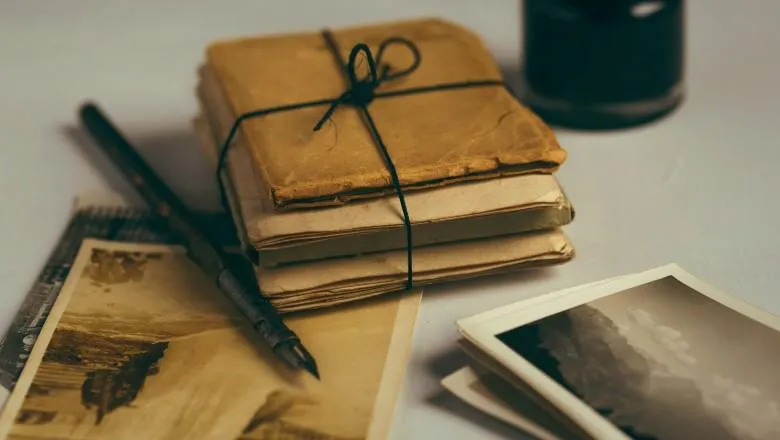 A stack of letters next to an old picture, a fountain pen and an ink container.